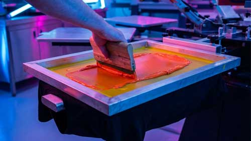 manos pasando rasero sobre camisa en taller serigrafia